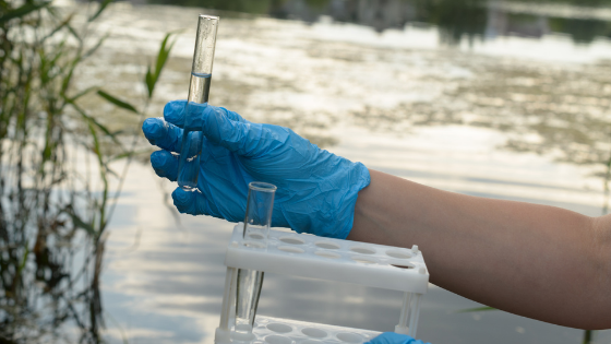 Pessoa com luvas azuis segurando tubos de ensaio na frente de um rio.